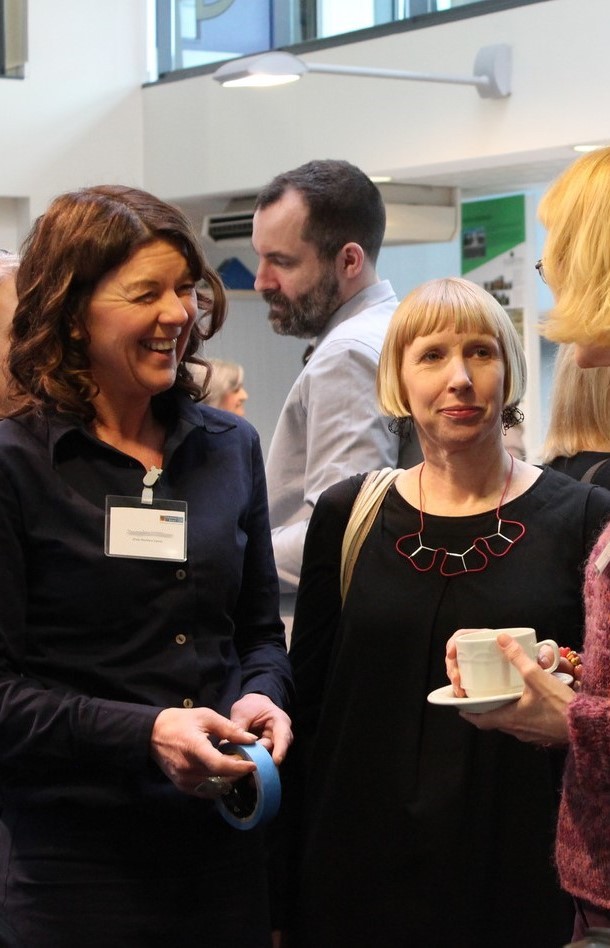 A group of people with names badges and cups of coffee stand and chat