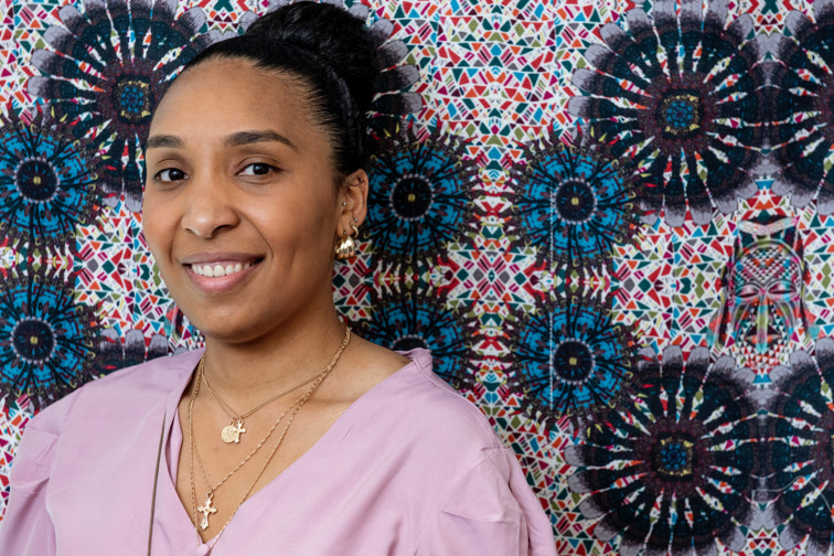 A young woman stands in front of some striking textiles of her own design
