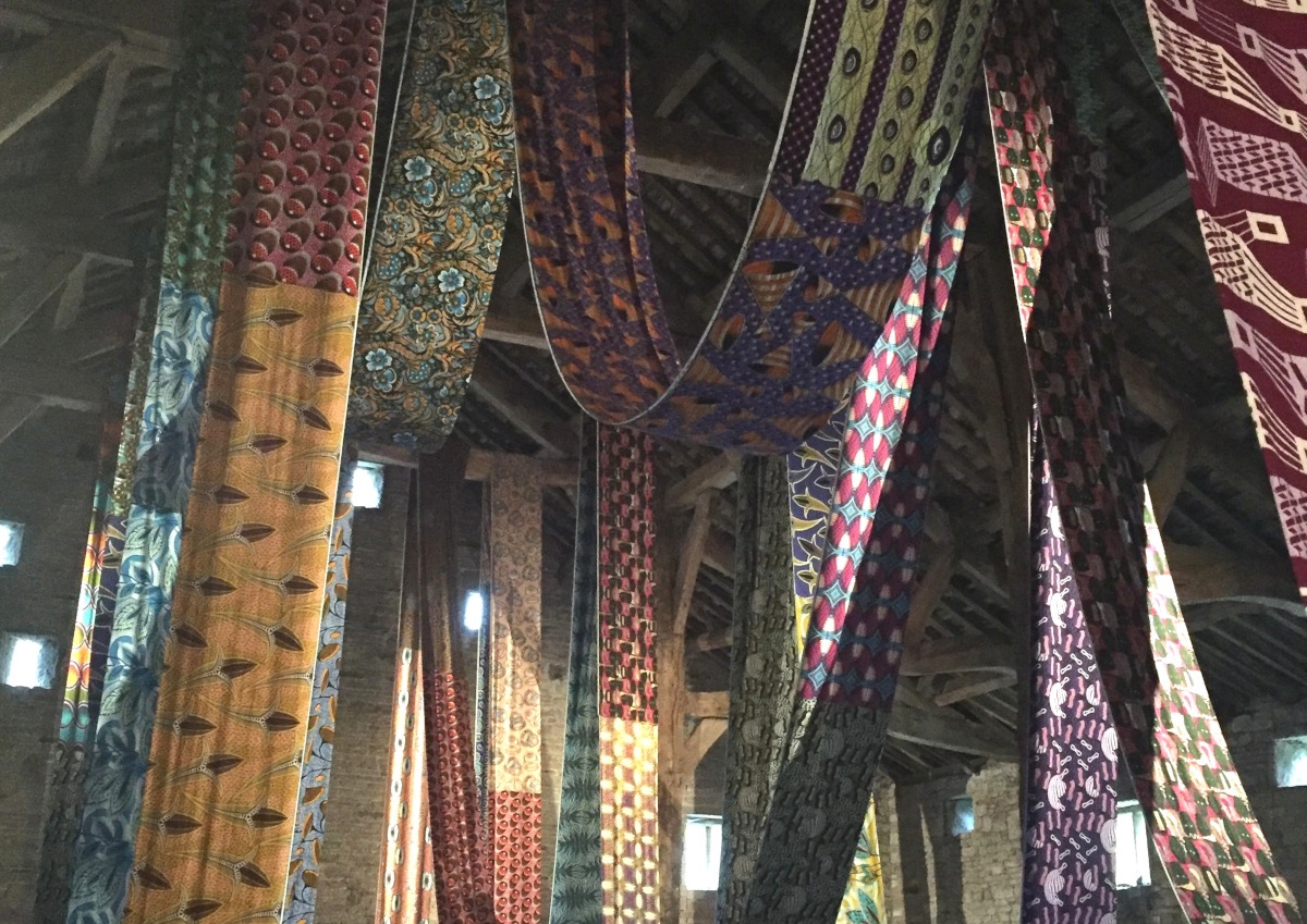 An art installation of strips of african print cloth hanging from the rafter of the Great Barn at Gawthorpe Hall. The work is by Lubaina Himid as part of The British Textile Biennial 2021