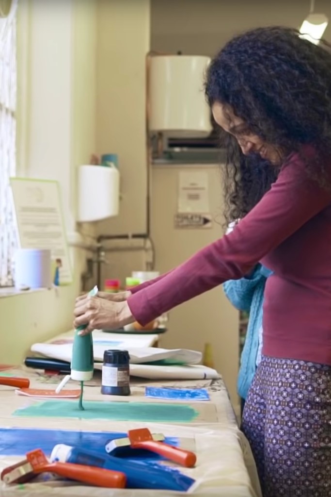 A young person squeezes green paint onto a screen in order to do a printing process